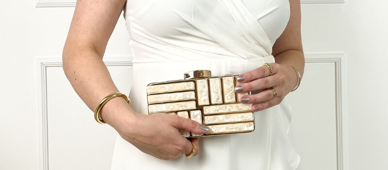 foto mostrando apenas o tronco de uma mulher, vestida de branco, segurando uma linda bolsa clutch de acrílico e metal, mostrando seu autocuidado e preocupação com moda.